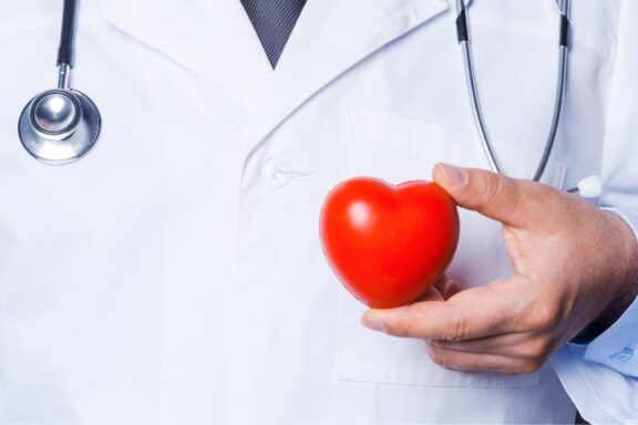 Kiedy udać się do kardiologa? Na zdjęciu lekarz trzyma czerwone serce.