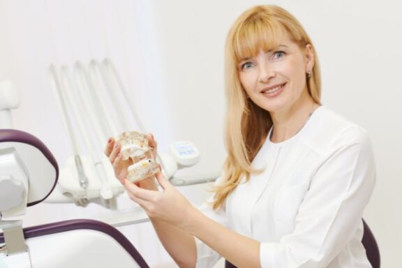 Pani lekarz ortodonta prezentuje sztuczną szczękę w gabinecie.