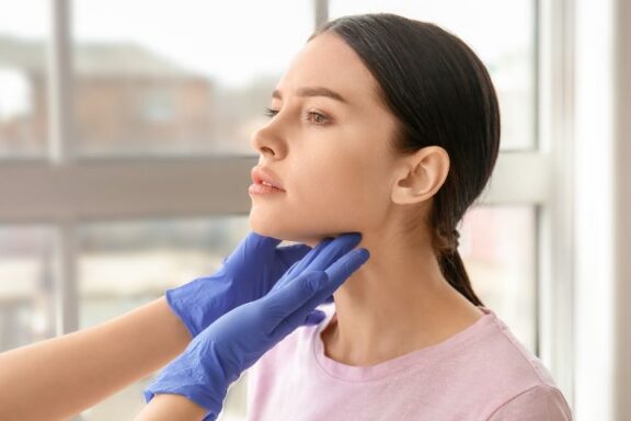 Endokrynolog badający palpacyjnie szyję młodej kobiety.