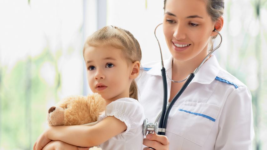 Pediatra osłuchujący plecy kilkuletniej dziewczynki trzymającej misia.