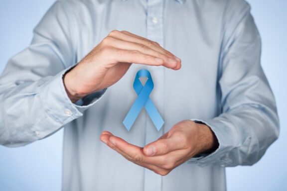 Niebieska wstążka — symbol raka prostaty, między osłaniającymi dłońmi